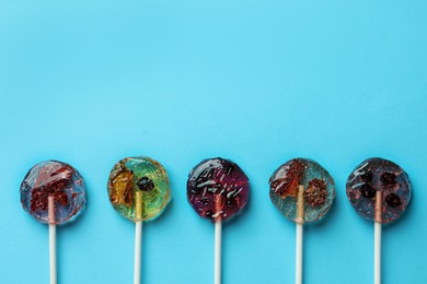 Photo of Sweet colorful lollipops with berries on light blue background, flat lay. Space for text