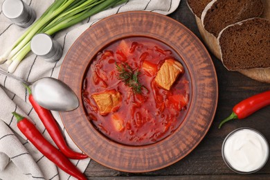 Bowl of delicious borscht, green onions, sour cream and chili peppers on wooden table, flat lay