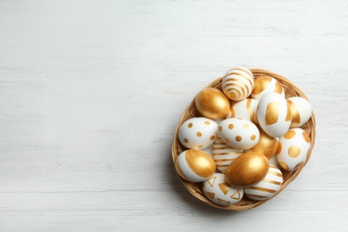 Wicker basket of traditional Easter eggs decorated with golden paint on wooden background, top view. Space for text