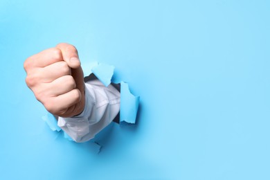 Photo of Businessman breaking through light blue paper with fist, closeup. Space for text