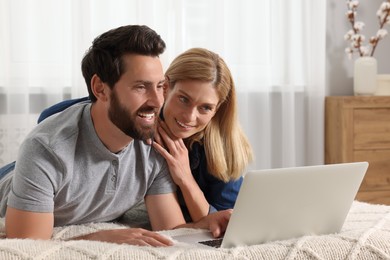 Photo of Happy couple with laptop on bed at home