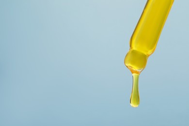 Photo of Dripping yellow serum from pipette on grey background, closeup. Space for text