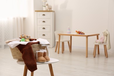 Photo of Laundry basket with baby clothes and crochet toys on white wooden table in child room, space for text
