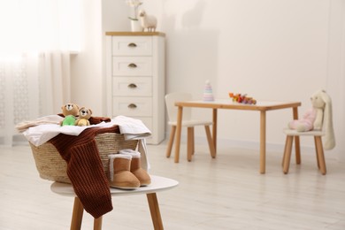 Laundry basket with baby clothes and crochet toys on white wooden table in child room, space for text