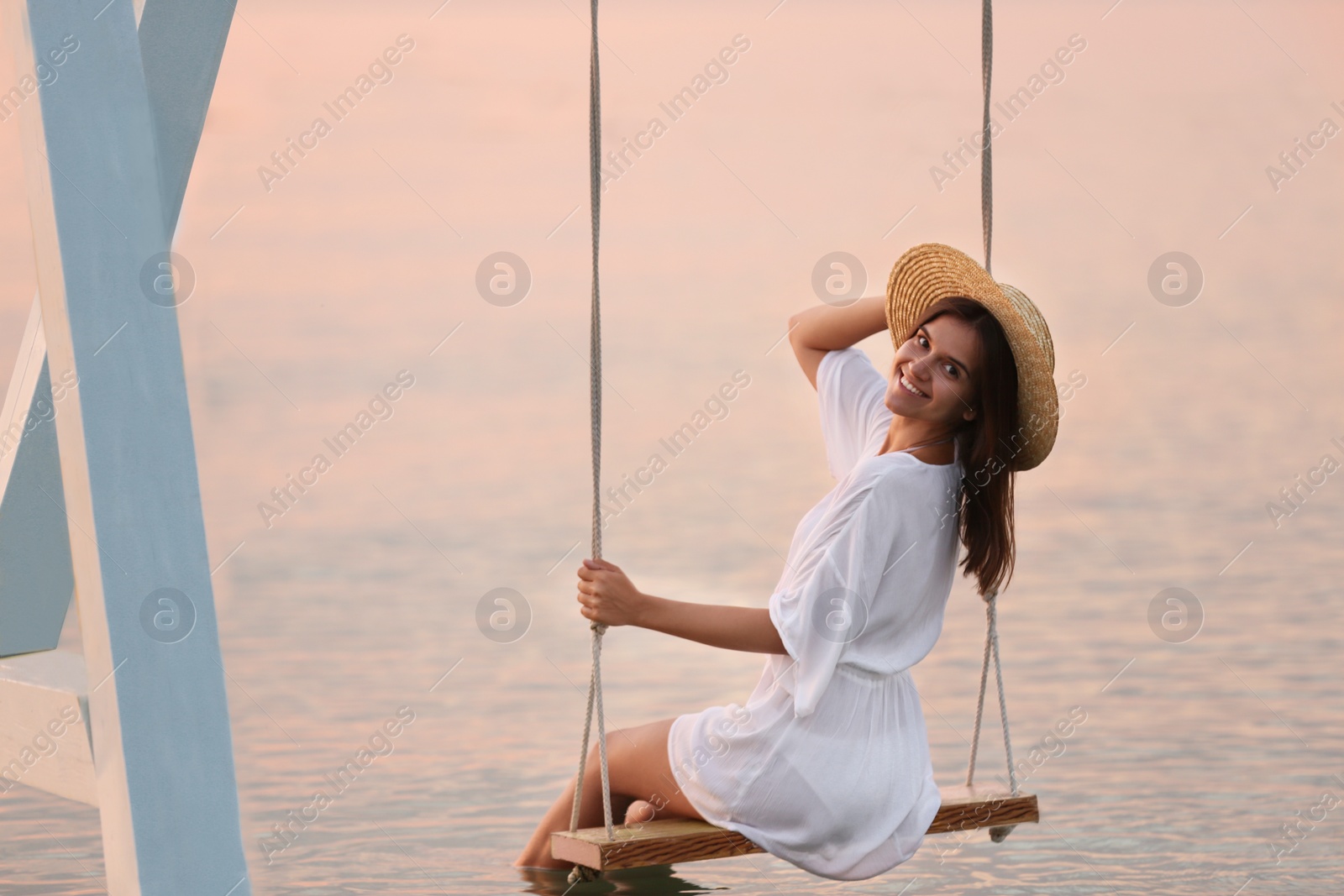 Photo of Young woman enjoying sunrise on swing over water