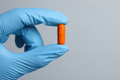 Doctor holding pill on grey background, closeup. Space for text