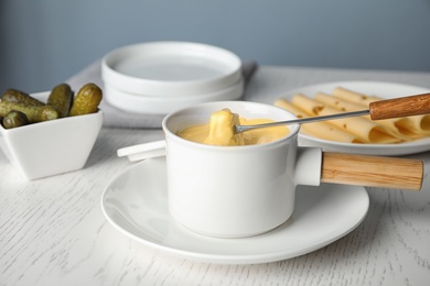 Photo of Pot of tasty cheese fondue and fork with bread on white wooden table