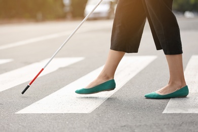 Blind person with long cane crossing road, closeup