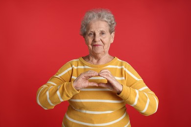 Photo of Elderly woman making heart with her hands on red background