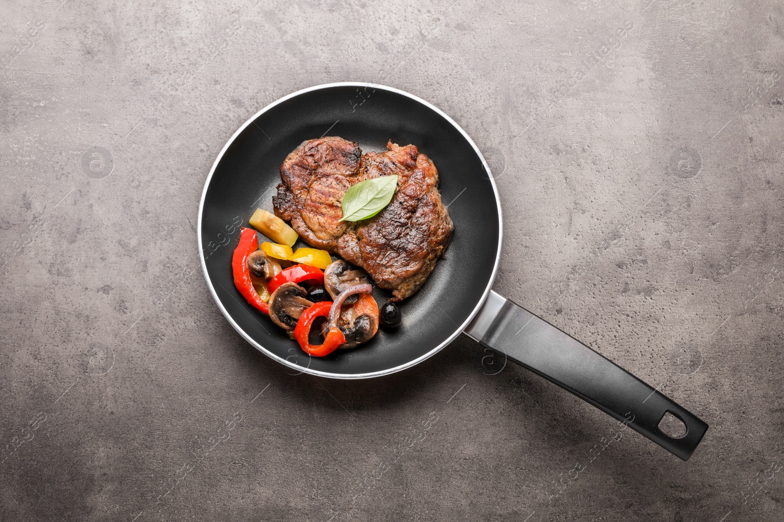 Photo of Frying pan with tasty steak and vegetables on grey table, top view