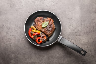 Photo of Frying pan with tasty steak and vegetables on grey table, top view