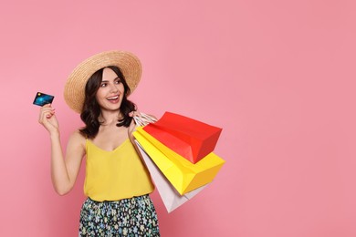 Photo of Beautiful young woman with paper shopping bags and credit card on pink background. Space for text