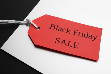Photo of Red tag with words BLACK FRIDAY SALE on color background, closeup