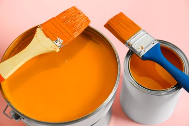 Photo of Bucket of orange paint, can and brushes on pink background, closeup