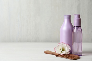 Different hair products, flower and comb on white wooden table. Space for text