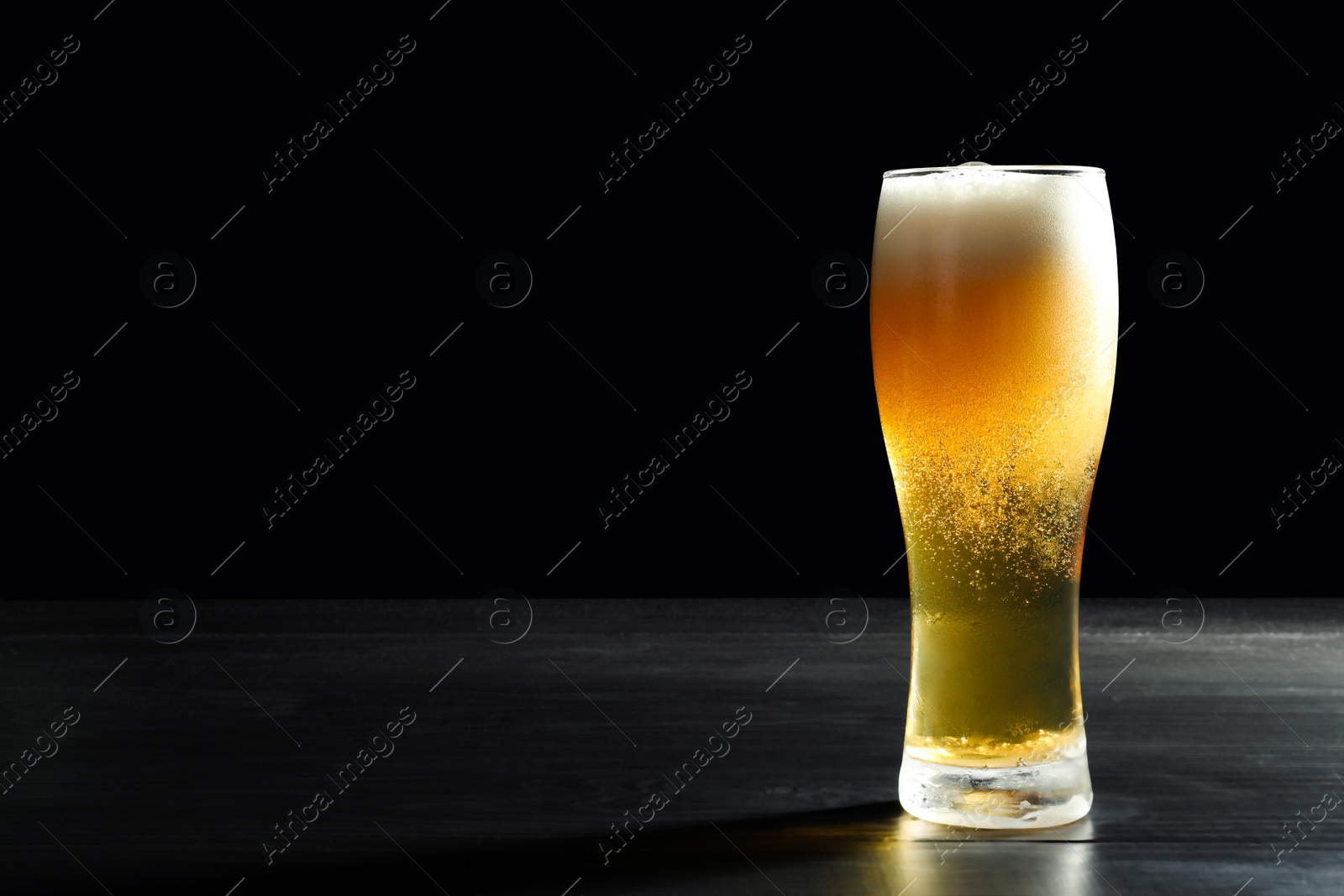 Photo of Glass with cold tasty beer on dark background