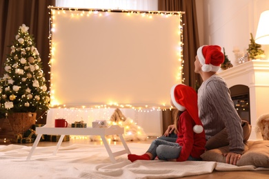 Photo of Father and daughter watching movie using video projector at home. Cozy Christmas atmosphere