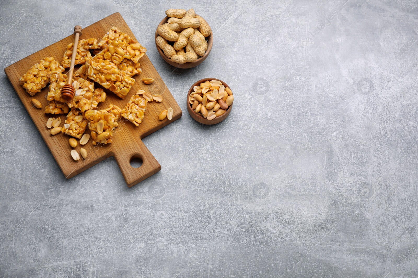 Photo of Delicious peanut kozinaki bars, nuts and honey dipper on light gray textured table, flat lay. Space for text