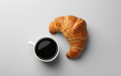 Delicious fresh croissant and cup of coffee on light background, flat lay