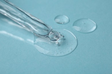 Pipette with cosmetic serum on light blue background, closeup