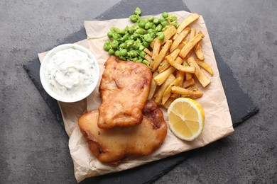 Tasty fish, chips, sauce and peas on grey table, top view