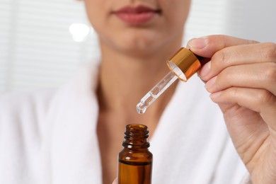 Photo of Woman with bottle of cosmetic serum and dropper on light background, closeup