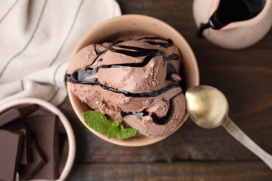 Bowl of tasty chocolate ice cream served on wooden table, flat lay