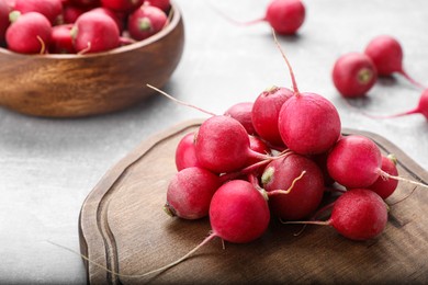 Wooden board with fresh ripe radishes on grey table, closeup