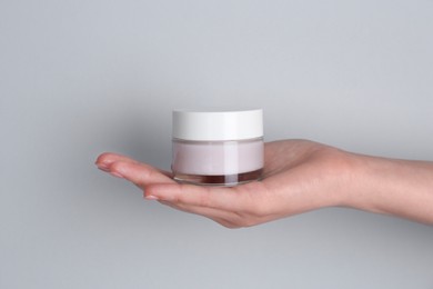 Woman holding jar of cream on grey background, closeup