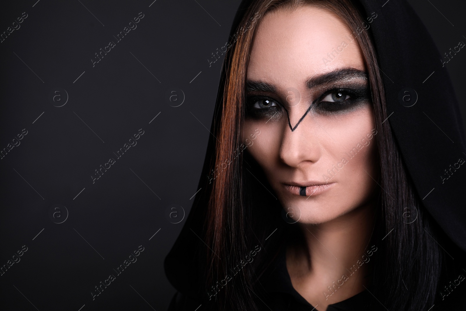Photo of Mysterious witch in mantle with hood on black background, closeup. Space for text