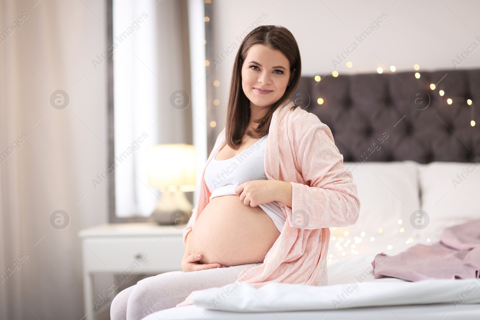 Photo of Beautiful pregnant woman sitting on bed at home