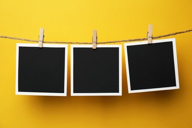 Photo of Wooden clothespins with empty instant frames on twine against yellow background. Space for text