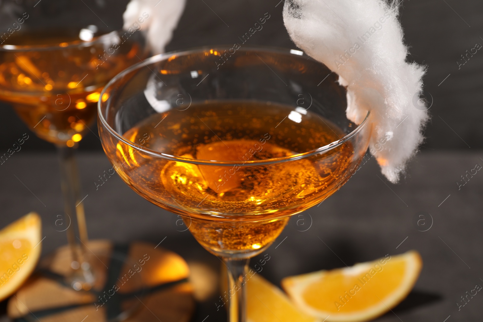 Photo of Tasty cocktails in glasses decorated with cotton candy on gray table, closeup