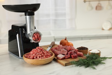 Photo of Electric meat grinder with beef and products on white marble table in kitchen