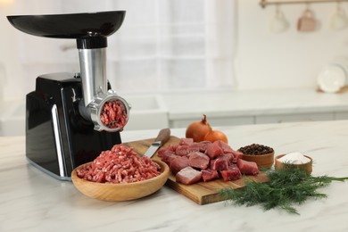 Electric meat grinder with beef and products on white marble table in kitchen