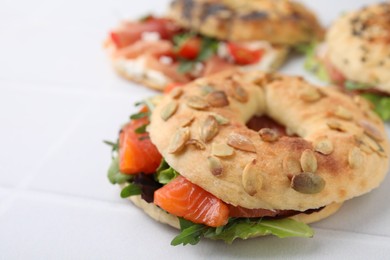 Tasty bagel with salmon and salad mix on white tiled table, closeup