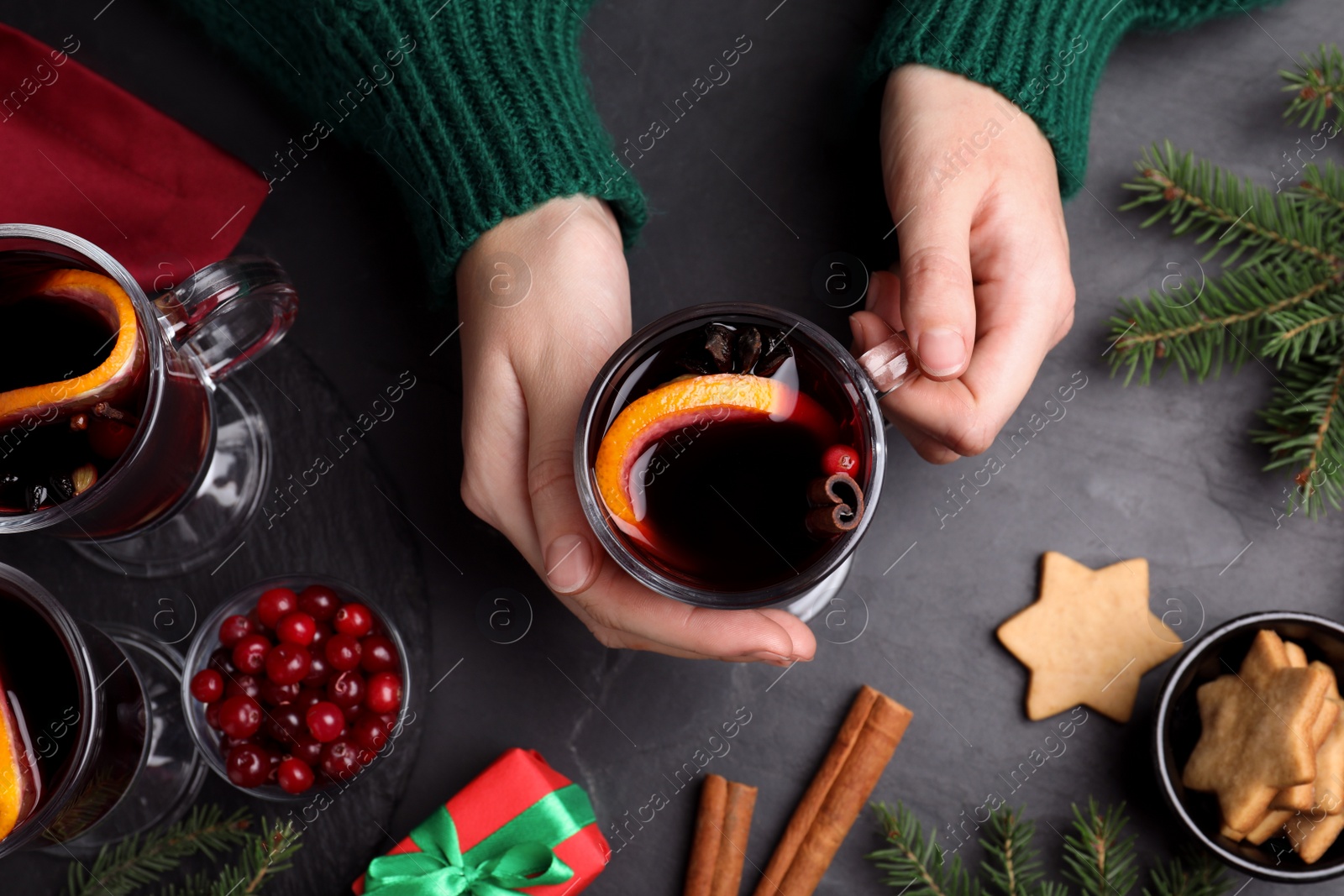 Photo of Woman with cup of aromatic mulled wine at black table, top view