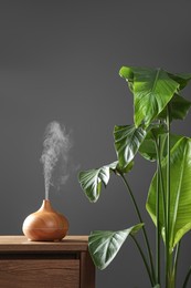 Photo of Air humidifier on chest of drawers near green houseplant against grey wall