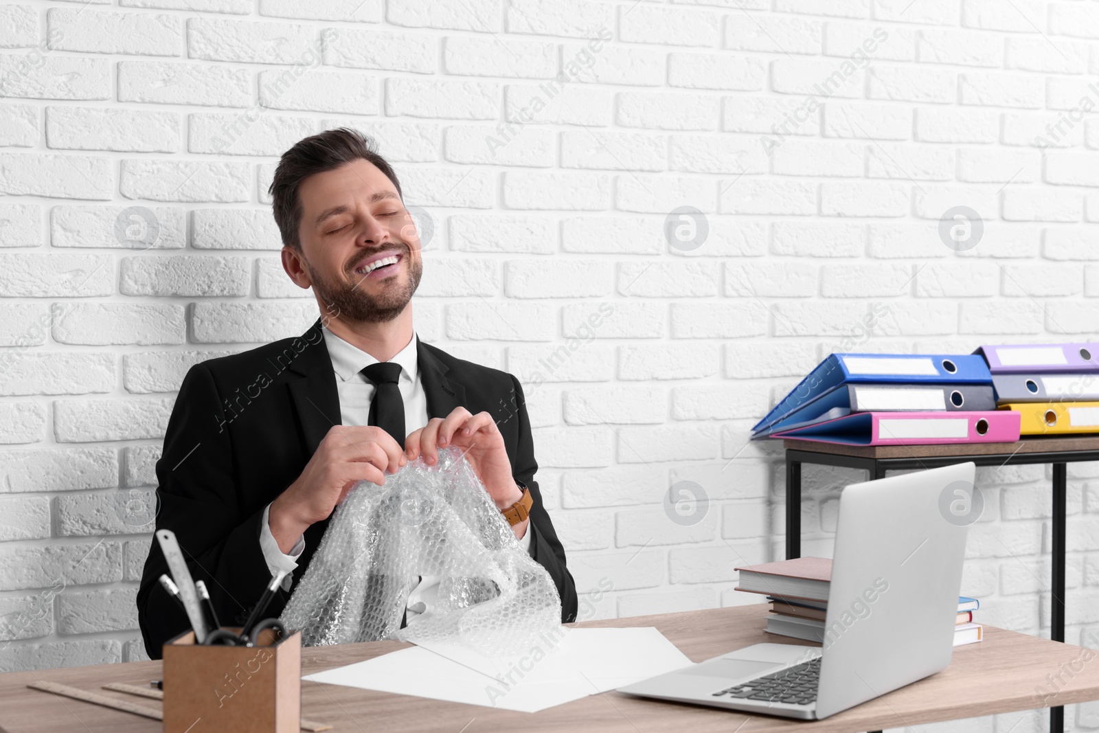 Photo of Businessman popping bubble wrap at workplace in office. Stress relief