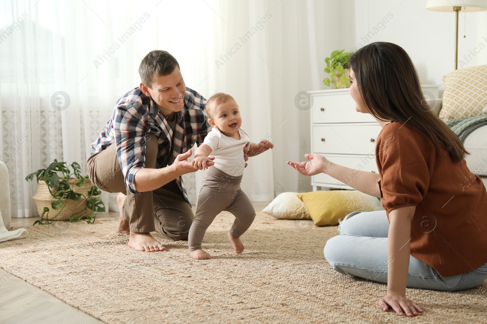 Photo of Parents supporting their baby daughter while she learning to walk at home