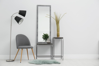 Photo of Stylish mirror and comfortable chair near white wall in room