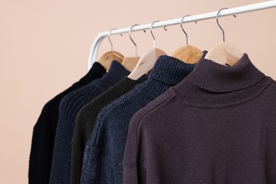 Photo of Rack with different warm sweaters on beige background, closeup