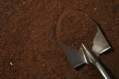 Photo of Metal shovel on fertile soil, top view and space for text. Gardening tool