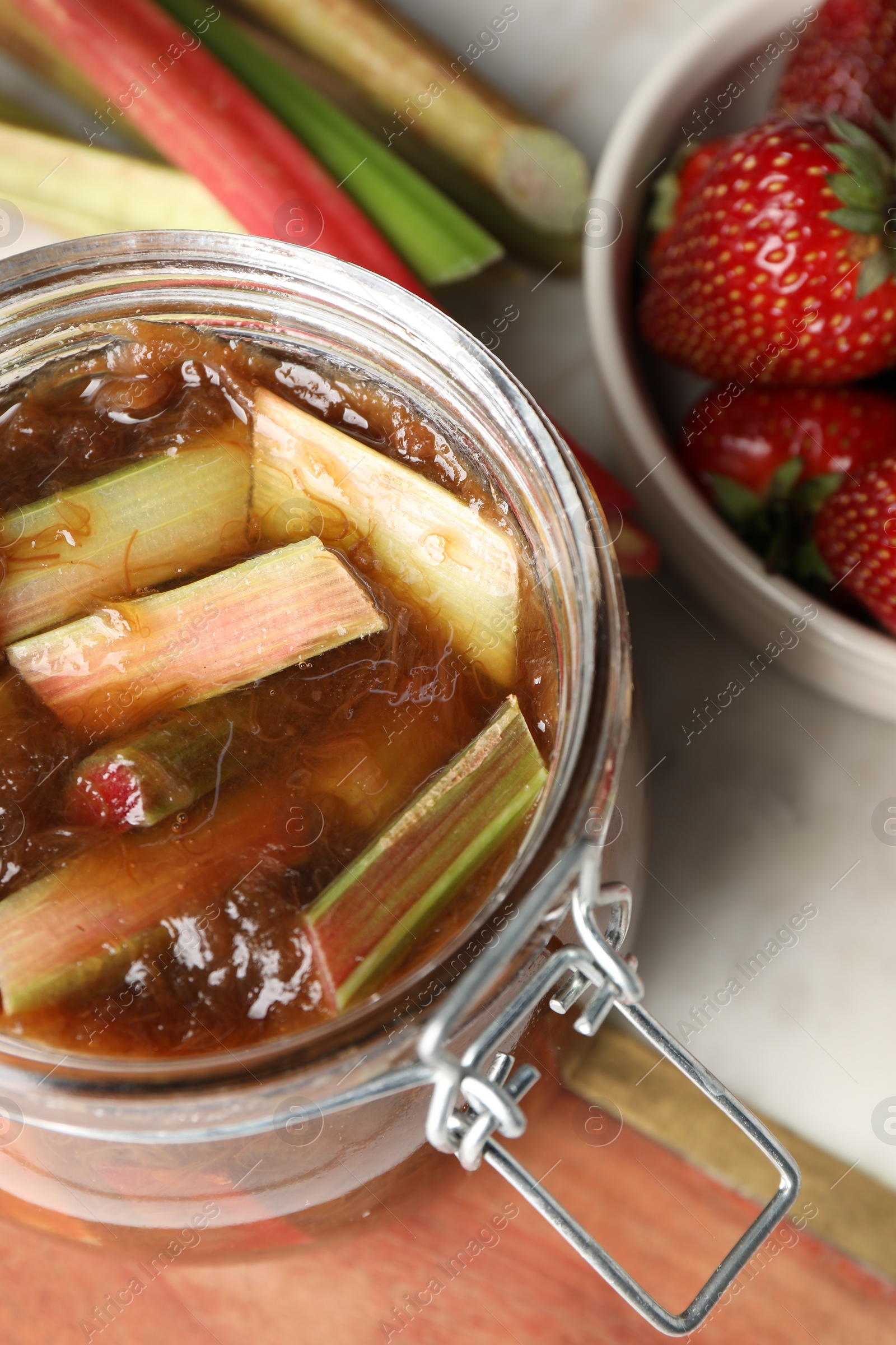 Photo of Jar of tasty rhubarb jam, fresh stems and strawberries on table, above view