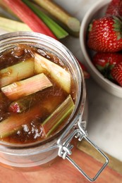 Jar of tasty rhubarb jam, fresh stems and strawberries on table, above view