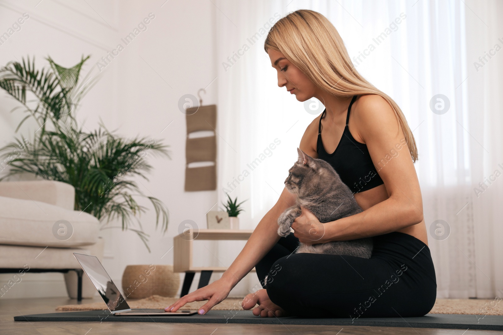 Photo of Beautiful woman with her cat watching online yoga class at home