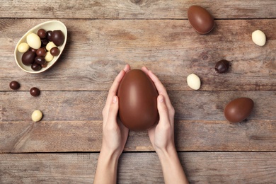 Photo of Woman holding chocolate Easter egg on wooden background, top view