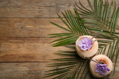 Photo of Fresh coconuts with drinking straws and flowers on wooden table, flat lay. Space for text