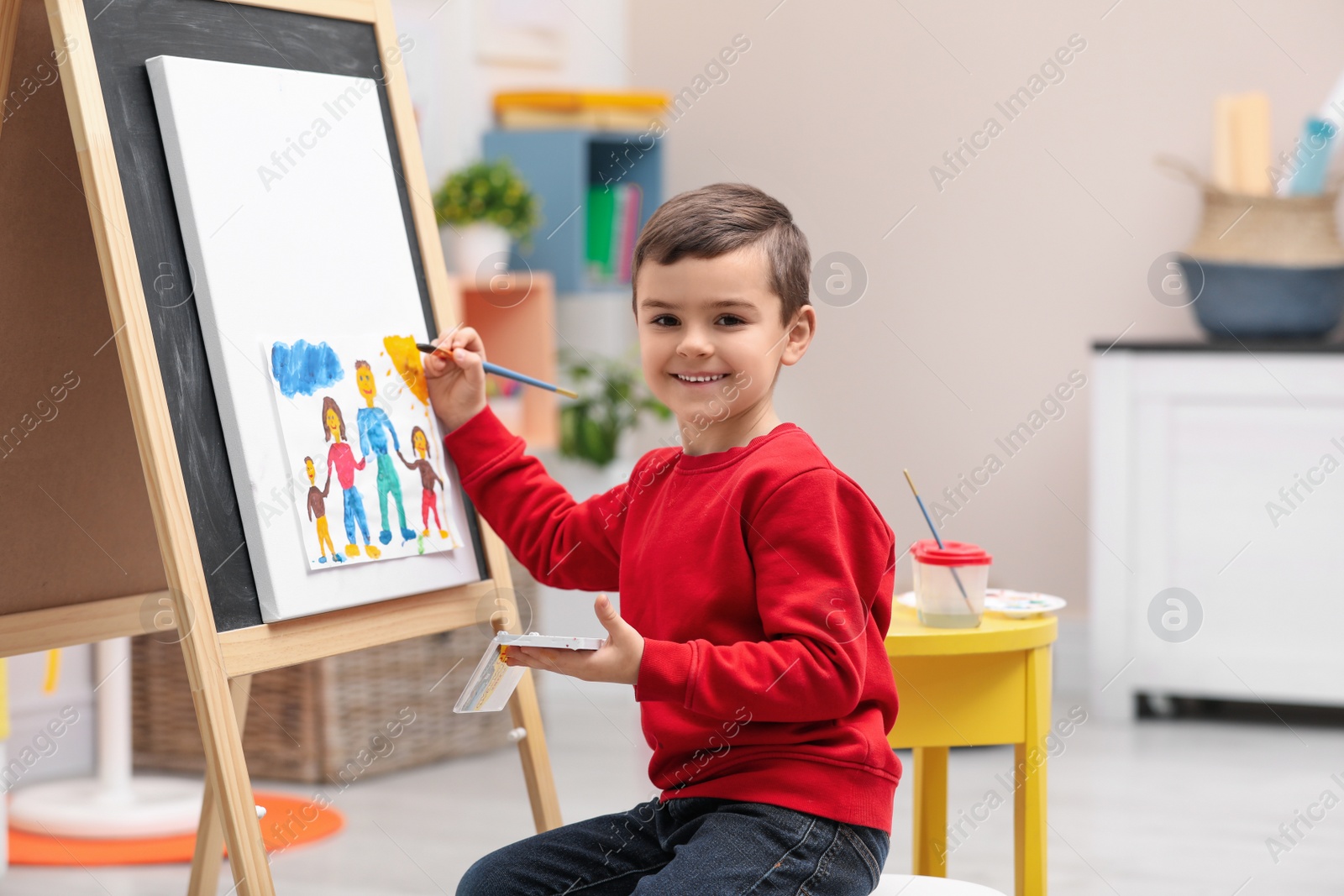 Photo of Little child painting on easel in room