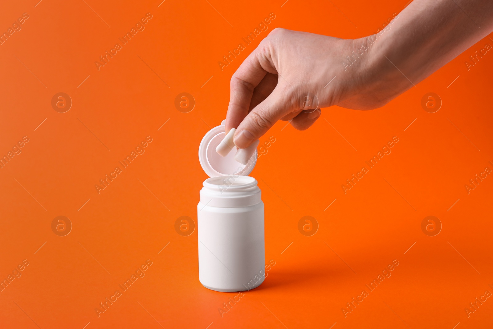 Photo of Woman taking chewing gums from jar on orange background, closeup